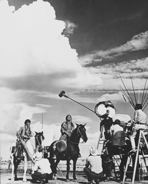 filmmakers operating a boom mic above two actors on horseback